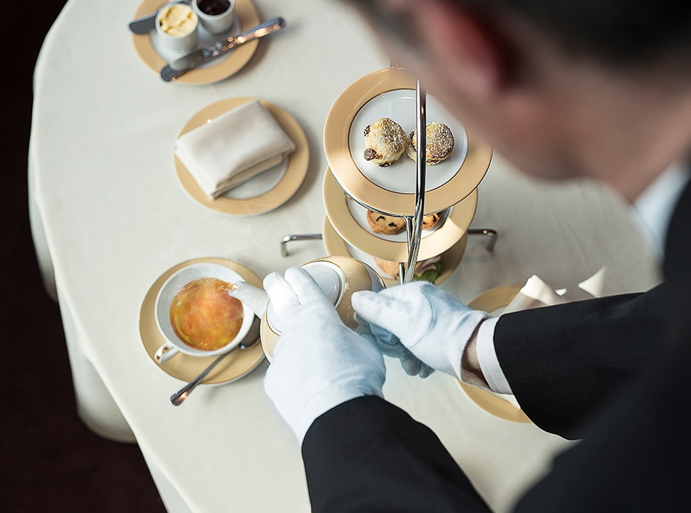 A MSC Yacht Club butler in white gloves serves cruises guests tea and coffee with delicious pastries on a tiered.